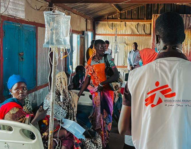 An MSF doctor in white vest walks past Sudanese internally displaced people in White Nile state, Sudan.