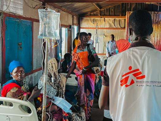 An MSF doctor in white vest walks past Sudanese internally displaced people in White Nile state, Sudan.