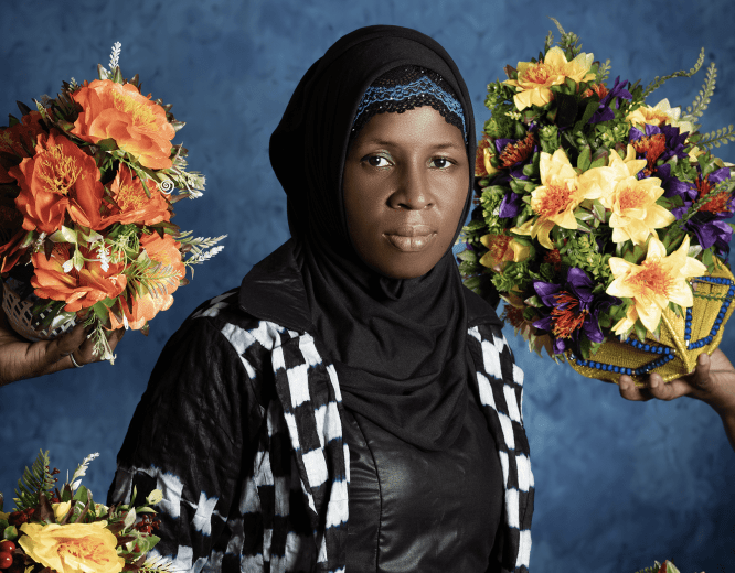 A woman in checker print dress surrounded by bouquets of flowers. 