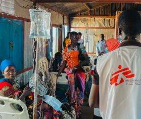 An MSF doctor in white vest walks past Sudanese internally displaced people in White Nile state, Sudan.